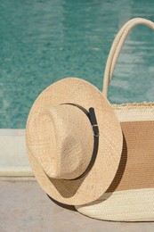 Stylish bag and hat near outdoor swimming pool on sunny day. Beach accessories