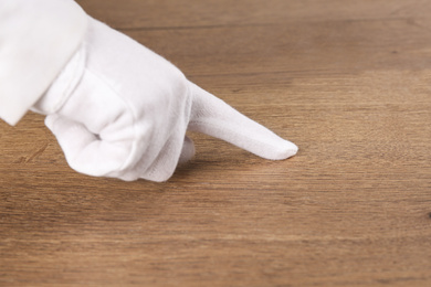 Person in white glove checking cleanliness of wooden  table, closeup