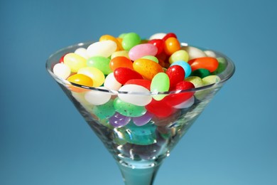 Photo of Beautiful martini glass with colorful candies on light blue background, closeup
