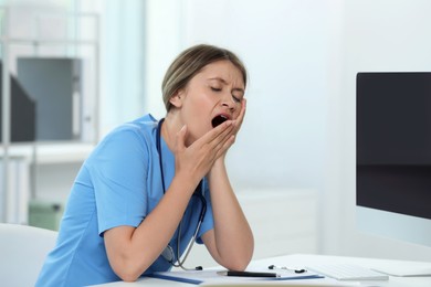 Exhausted doctor yawning at workplace in hospital