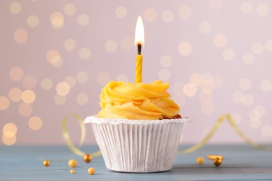 Tasty birthday cupcake on light blue wooden table against blurred lights