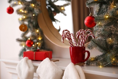 Candy canes in cup near mirror with Christmas garland, closeup