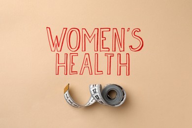 Measuring tape near words Women's Health on beige background, top view
