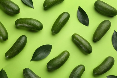 Photo of Whole seedless avocados with leaves on green background, flat lay