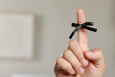 Man showing index finger with tied bow as reminder on blurred background, closeup. Space for text
