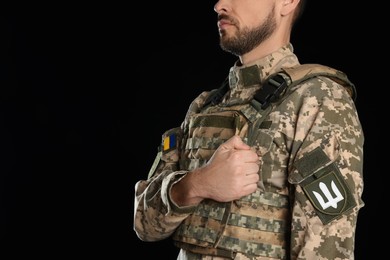 Soldier with Ukrainian trident on military uniform against black background, closeup. Space for text