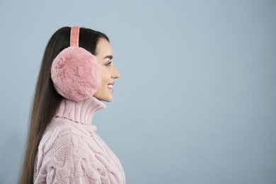 Beautiful young woman wearing earmuffs on light grey background. Space for text