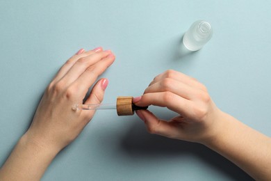 Photo of Woman dripping serum from pipette on her hand at white table, top view