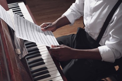 African-American man with note sheets at piano indoors, closeup. Talented musician