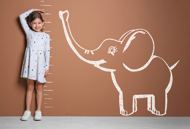 Little girl measuring height and drawing of elephant near brown wall