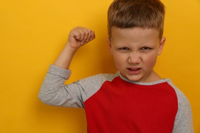 Photo of Angry little boy on yellow background. Aggressive behavior
