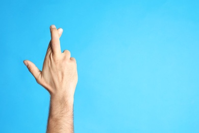 Man with crossed fingers and space for text on light blue background, closeup. Superstition concept