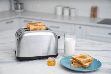 Modern toaster with slices of bread, honey and milk on white marble table in kitchen
