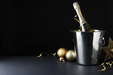 Happy New Year! Bottle of sparkling wine in bucket and festive decor on table against black background, space for text