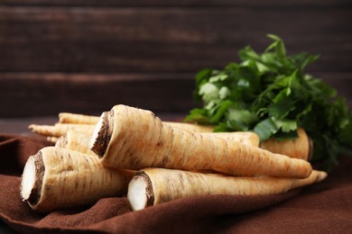 Photo of Whole raw parsley roots and fresh herb on brown fabric, closeup