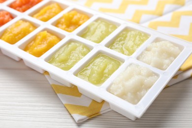 Different purees in ice cube tray on white wooden table, closeup. Ready for freezing