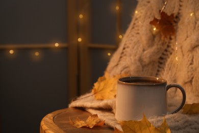 Cup of aromatic tea, sweater and autumn leaves on wooden chair indoors, space for text
