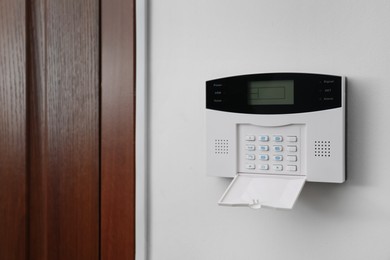 Home security alarm system on white wall near door, space for text