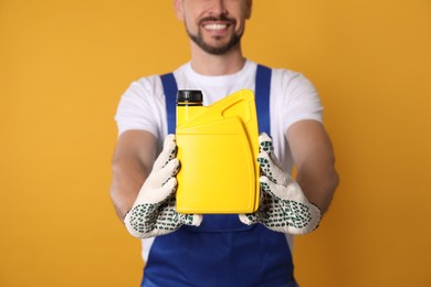 Man showing yellow container of motor oil on orange background, closeup