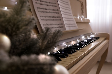 White piano with festive decor and note sheets indoors, closeup. Christmas music
