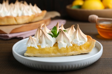 Piece of delicious lemon meringue pie with mint served on wooden table, closeup