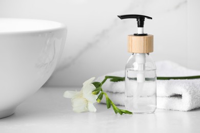 Bottle with dispenser cap, towel and beautiful flower on white table in bathroom, closeup