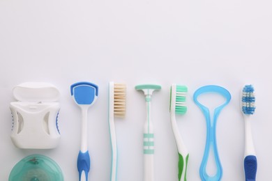 Different tongue cleaners, dental flosses and toothbrushes on white background, top view