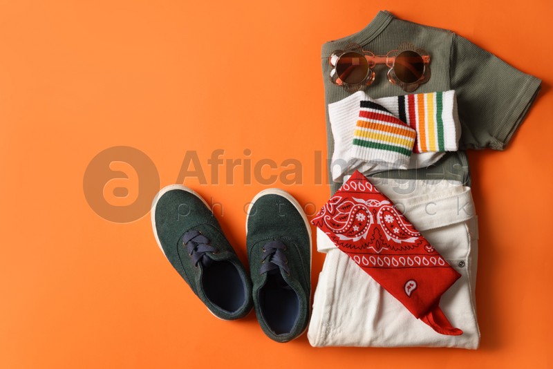 Stylish child clothes, shoes and accessories on orange background, flat lay. Space for text