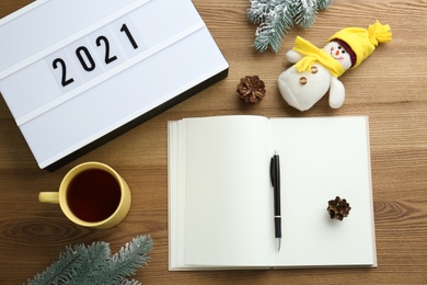 Light box with number 2021 near notebook, new year goals. Flat lay composition on wooden table