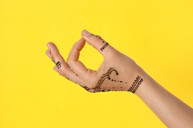 Woman with henna tattoo on hand against yellow background, closeup. Traditional mehndi ornament