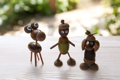 Photo of Cute figures made of acorns on white wooden table