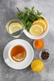 Cup with delicious immunity boosting tea and ingredients on grey table, flat lay