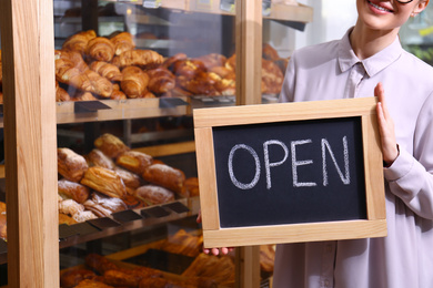 Photo of Female business owner holding OPEN sign in bakery, closeup