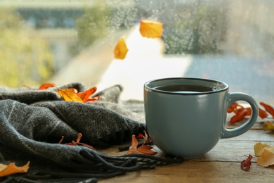 Cup of hot drink and autumn leaves near window on rainy day. Cozy atmosphere