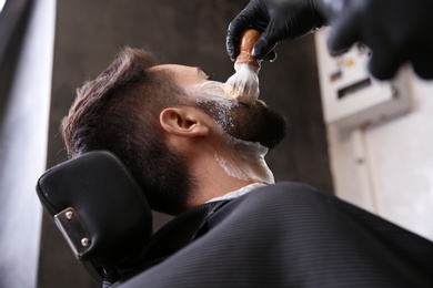 Professional hairdresser applying shaving foam onto client's skin in barbershop