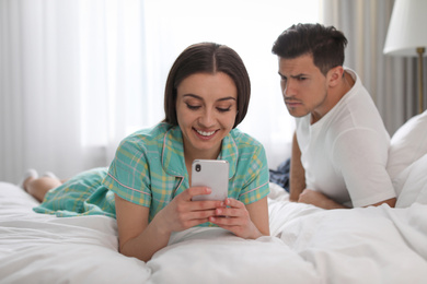 Photo of Distrustful man peering into girlfriend's smartphone at home. Jealousy in relationship