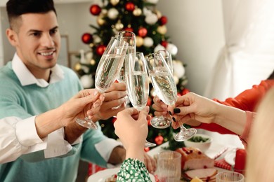 Family with their friends clinking glasses at festive dinner indoors. Christmas Eve celebration