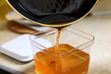 Pouring used cooking oil from frying pan into container on beige table, closeup