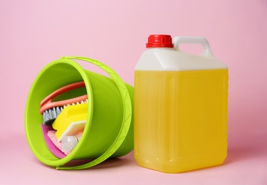 Green bucket with tools and canister of detergent on pink background. Cleaning supplies