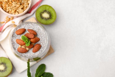 Photo of Delicious dessert with chia seeds, almonds and fresh cut kiwi fruits on light table, flat lay. Space for text