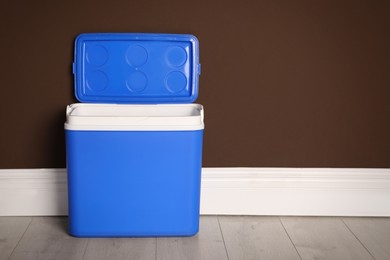 Open blue plastic cool box near brown wall. Space for text