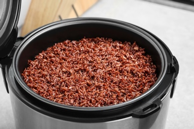 Modern multi cooker with boiled brown rice in kitchen, closeup