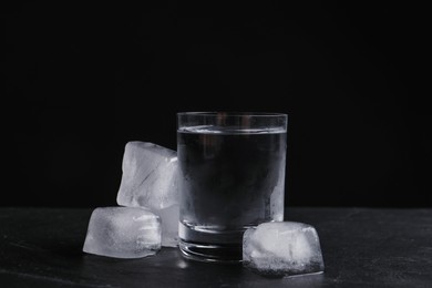Vodka in shot glass with ice on table against black background