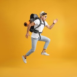 Emotional male tourist with travel backpack jumping on yellow background