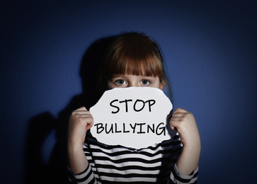 Abused little girl with sign STOP BULLYING near blue wall