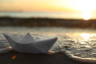 Sea wave carrying away white paper boat at sunset, space for text. Bokeh effect