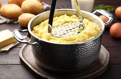 Mashing potatoes in pot on wooden table, closeup