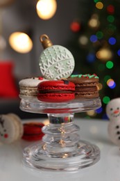 Photo of Beautifully decorated Christmas macarons on white table against blurred festive lights