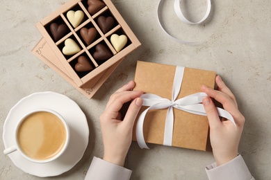 Woman with box of heart shaped chocolate candies and coffee at light table, top view