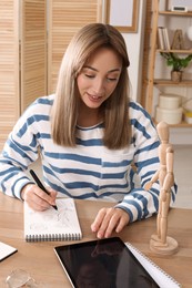Woman drawing in sketchbook with pen at wooden table indoors
